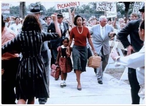 November 1960 - Ruby Bridges holds tightly to her mother’s hand as she enters into an angry mob to c