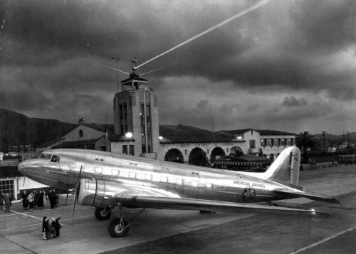 A shining DC-3 parked in front of the Grand Central Airport terminal as night falls, Glendale, California, 1940’s.