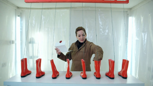 [ID: Five screencaps from Taskmaster. Katherine Parkinson stands in a white room, in front of a tabl