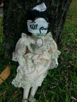 bizarreismm:  Found sitting against a tree on a busy street in Singapore was a blindfolded doll, dressed in a dirty, lacy outfit. Written on the blindfold was the Arabic word “bismillah”, which when translated means, “in the name of Allah.” Photos