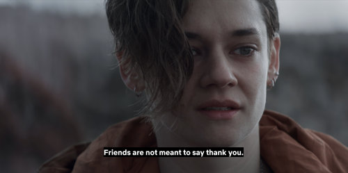 Text reads: Friends are not meant to say thank you. A close-up of a white woman with blue eyes and brown hair that partially obscures her face. She wears multiple small, silver earrings and a rust-coloured jacket. The background is dull and grey.