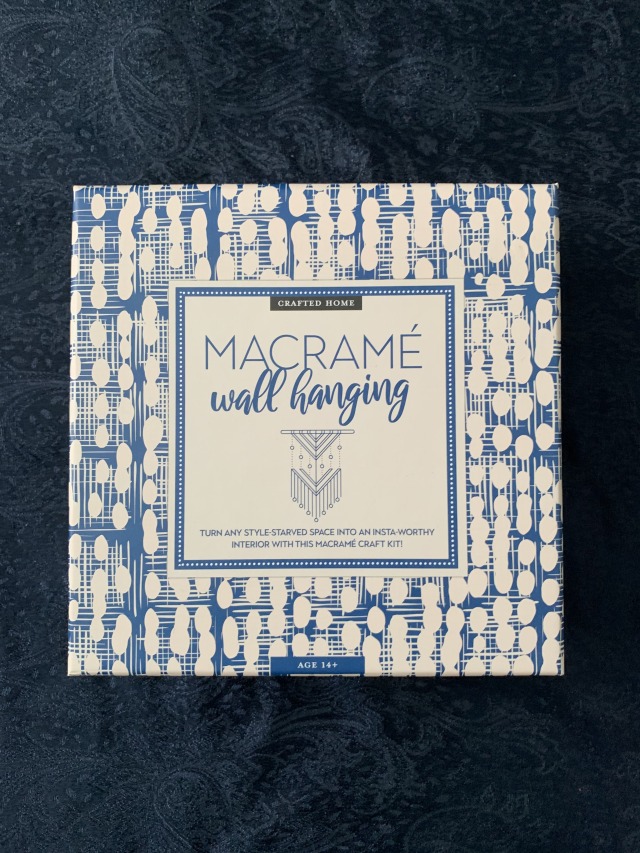Photo of a blue and white box for a macrame kit, against a navy background. Blue cursive text on a white label in the centre reads: "Crafted Home - Macrame wall hanging" above a simple outline illustration of the hanging design. Smaller text underneath reads: "Turn any style-starved space into an Insta-worthy interior with this macrame craft kit!".