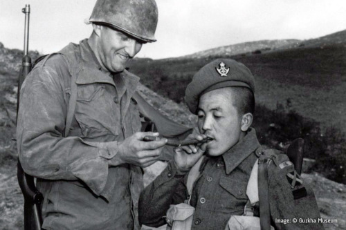 An American GI and a Gurkha soldier share cigars in Italy during World War II.  Dated 1944.