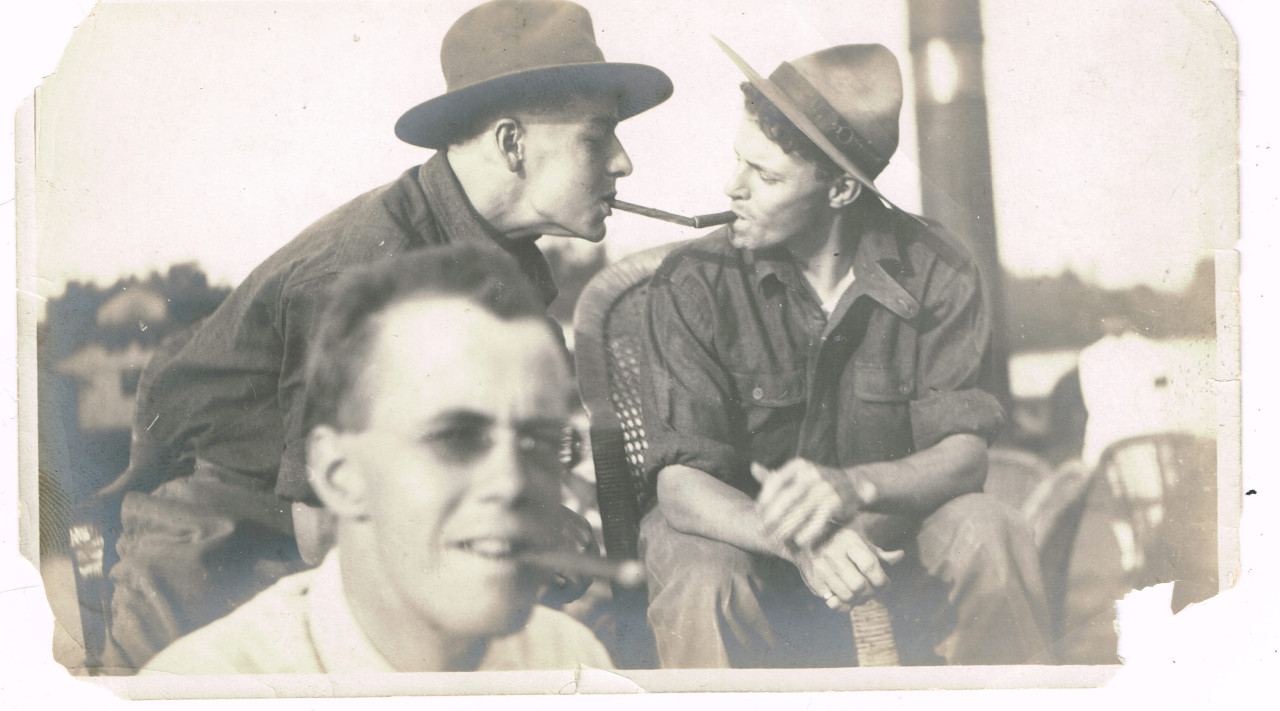 A vintage photo of two gay cowboys lighting each other's cigars.