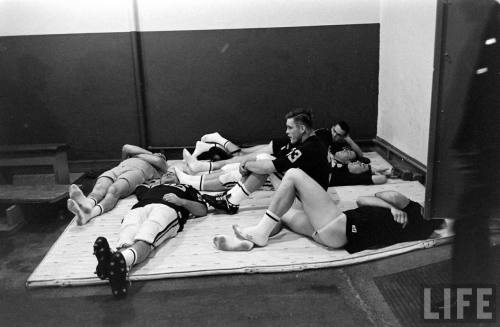 College football players in repose before a Minnesota-Iowa game, 1960. Three of the players are hang