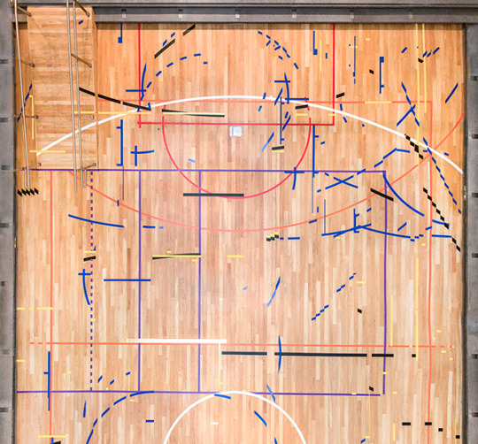 Aerial view of a multi-sports indoor court with colorful pieces of tape on it.
