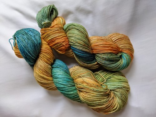 two skeins of yarn that have distinct patches of sunflower yellow and an almost-sky blue, with bits of green between them. the colours, especially the yellow, are lightly speckled with darker greens and orangey reds.