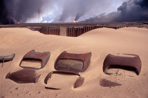 biladal-sham:  Kuwait. Car cemetery. In the background: burning Burgan oil fields set on fire by retreating Iraqi troops. 1991. A. Abbas 