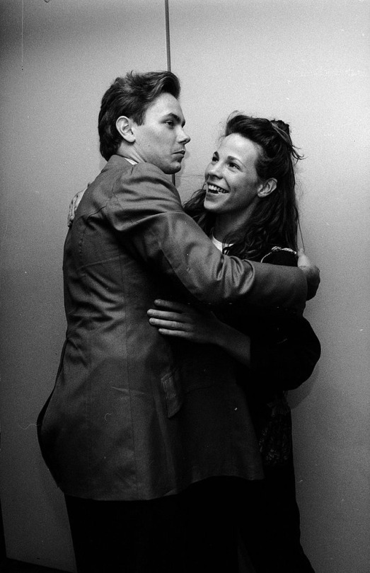 river phoenix & lili taylor at the dogfight premiere in september 1991. river has his arms around her and they are both smiling. river looks to be mid-sentence.