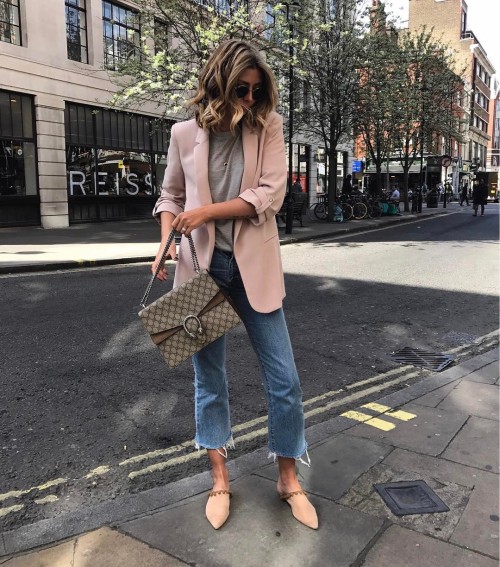 Emma Hill is wearing a blazer in a playful shade of pale pink, paired with roughly cut-off deni