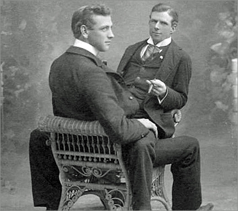 A vintage photograph of two men. One man sits on the lap of the other.