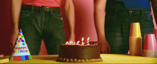 Present Danny bends to blow out the candles on his birthday cake. Arin Hanson is standing beside him with his upper half out of frame.