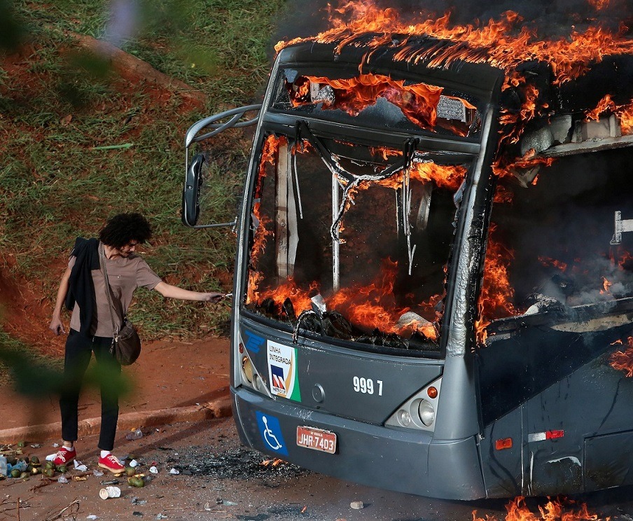 internetbynight: A man lights up his cigarette with the flames of a bus burned by