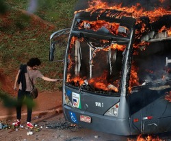 internetbynight: A man lights up his cigarette with the flames of a bus burned by anti-government demonstrators in Brazil