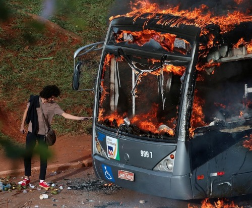 internetbynight:A man lights up his cigarette with the flames of a bus burned by anti-government dem