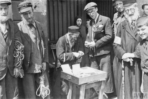 Warsaw Ghetto (Poland, 1941):An elderly Jewish woman selling her scarce possessions in the street.A 