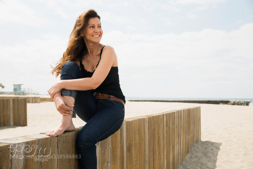 Smiling barefoot woman sitting on beach wall