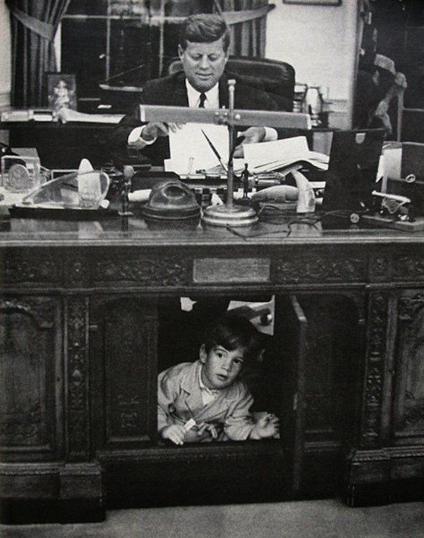 historicaltimes:  JFK Jr. peers out from the panel in his father’s desk in the