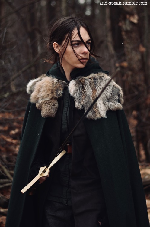 and-speak:they/them[image description: photo of op standing outside in the woods from the thighs up. they wear a dark green tunic, dark grey pants, brown belt and long brown suede vest, and a dark green cloak with a fur mantle. op is a white person with