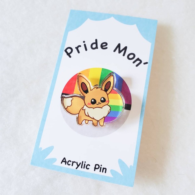 a rainbow eevee pin with a blue and white card backing with the words "Pride mon'" and "acrylic pins." 