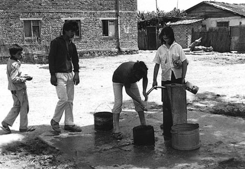 Albanians drawing water from a spigot on a state farm in central Albania . 90s. Sudetic