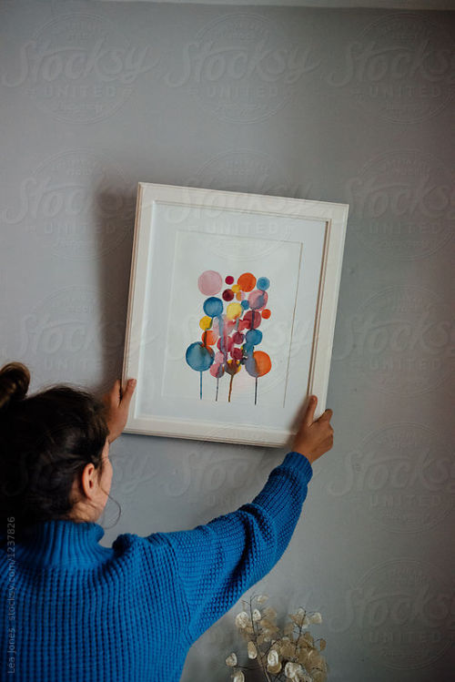 young lady hanging her art on the wall By LeaJonesAvailable to license exclusively at Stocksy 