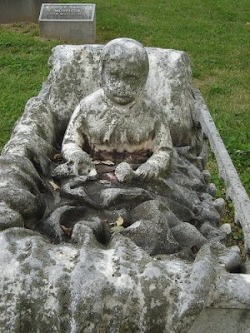 A sculpture of a child in a crib, covered with a blanket of stone.