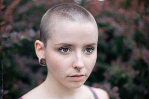 A girl with a shaved head and red bushes in the background By erikn_nAvailable to license exclusivel