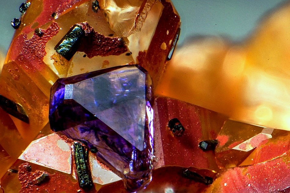 underthescopemin:  Fluorite, Quartz A small octahedral crystal cube of purple Fluorite,  red prisms