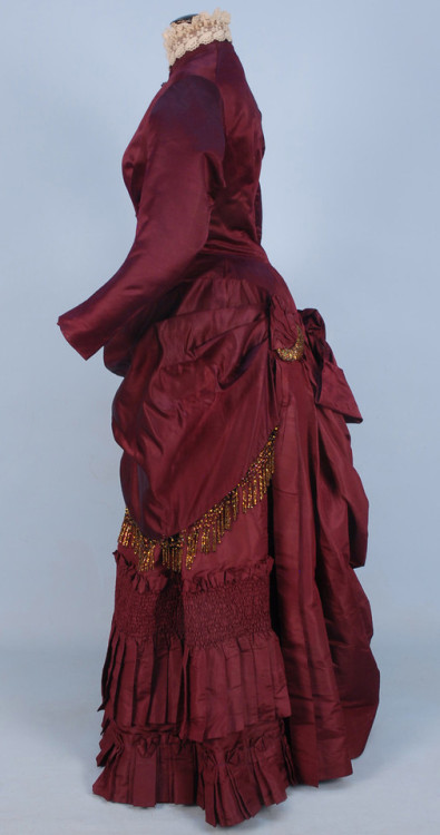 SILK BUSTLE DRESS with BEADED TRIM, c. 1880. 2-piece claret satin and taffeta having fringe, buttons