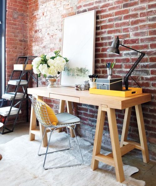 Add warmth to an industrial space with a wooden desk, plush rug and an elegant flower arrangement.