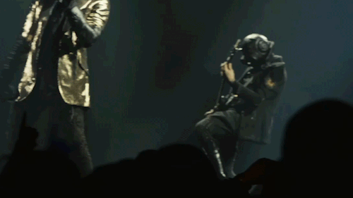 Phantom Ghoul plays the guitar behind papa on stage. He head-bangs and leans back as he plays.