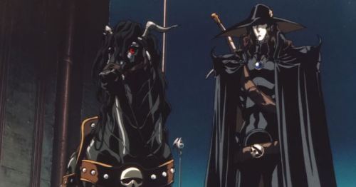 A man, the vampire hunter D, is standing next to his horse. Both are very shiny and dressed in leather and metal. D is on the right and the armored horse is on the left. They are both in all black because this is a dramatic goth movie.