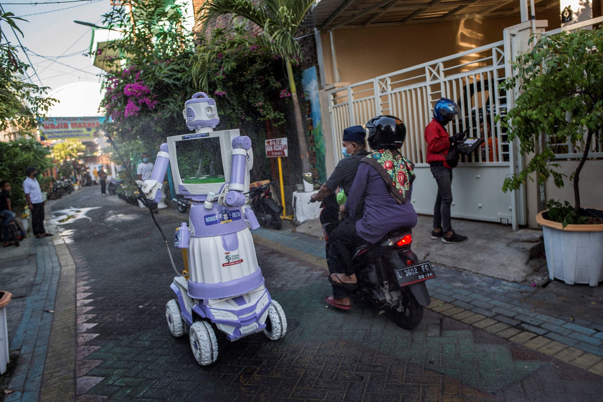 A cream and purple robot made from upcycled parts passing a couple on a scooter in a paved lane