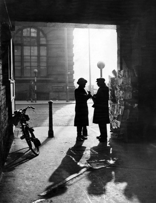 Mirrorpix. A man talking to a newspaper seller under the covered entrance to Leather Lane, off Dale 