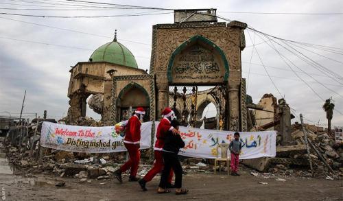 Iraqi youths dressed in Father Christmas suits walk with children by the ruins of the Great Mosque o