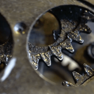 a gif. closeup of an old rusted mechanism, with lots of gears turning. the gears at the front have spaces in them so the gears behind can be seen.