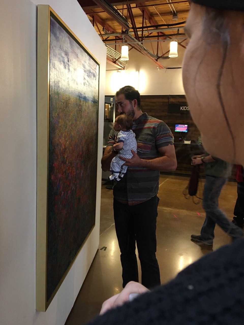 jafaaar:    A man holding his baby up to paintings and talking to him at an art gallery  