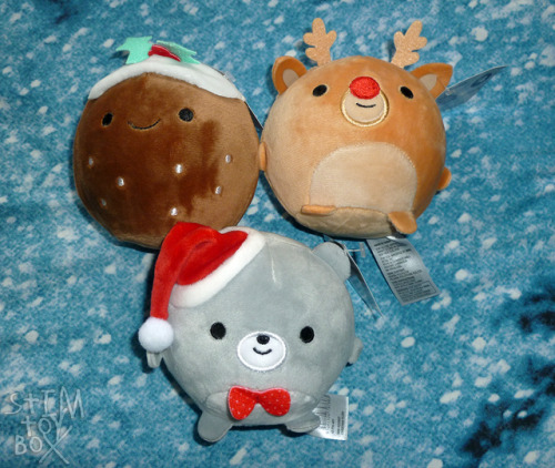 [image description: three Christmas-themed squishy plush sitting on a mottled blue, white and black 