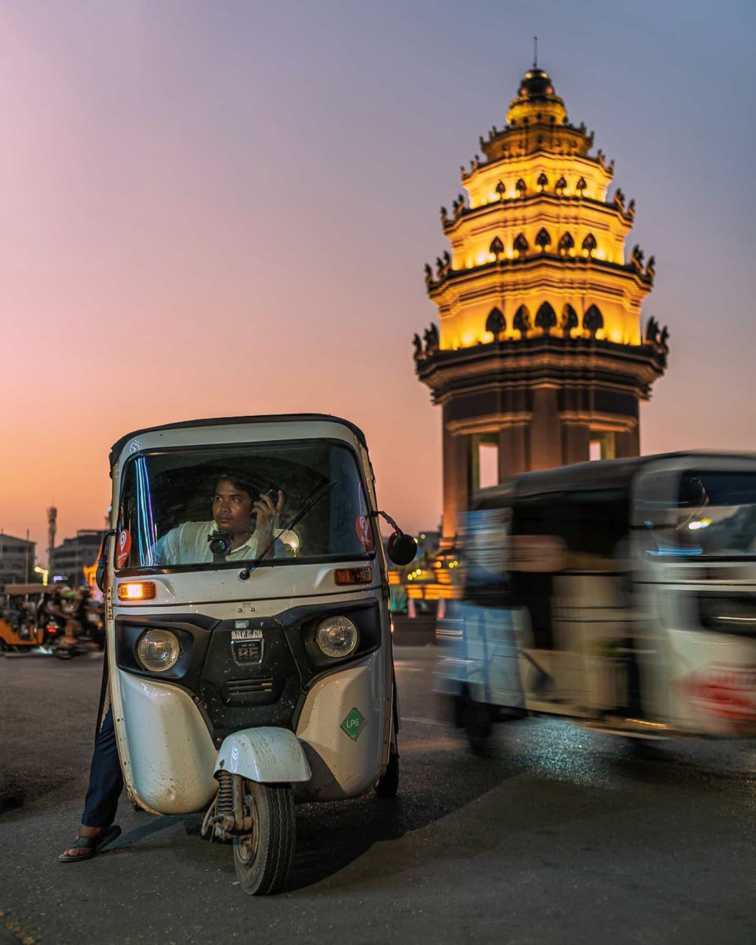 A photograph of Cambodia’s Independence monument as a local Pass App and Grab Tuk Tuk/taxi driver waits for a customer in the busy Valentine’s Day traffic.