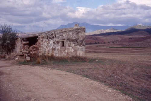 Paisaje navarrenjo con un edificio de piedra en ruinas y castillos en las colinas lejos, 1998.