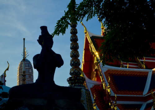 A statue with a temple from Wat Pho, or the Temple of the Reclining Buddha, in the background.