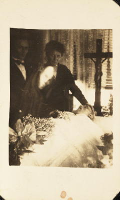 weirdvintage:  Ghostly mourning scene, c 1920 by William Hope, “spirit photographer” A woman mourns for her husband in a Chapel of Rest, the woman’s son stands beside her.  The image of a man’s face has been superimposed over the original photograph.