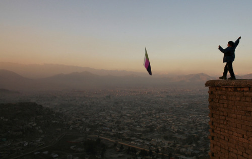 mvtionl3ss: A boy flies a kite along a hill overlooking the city of Kabul at sunset.