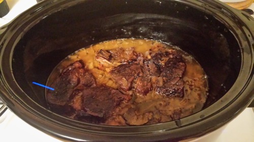 A cooked pot roast, sitting in light brown juices in a slow cooker.