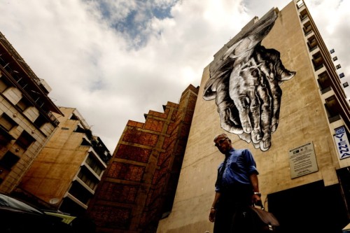 A man walks down a street with a turned upside down mural inspired on “The Praying Hands&rdquo