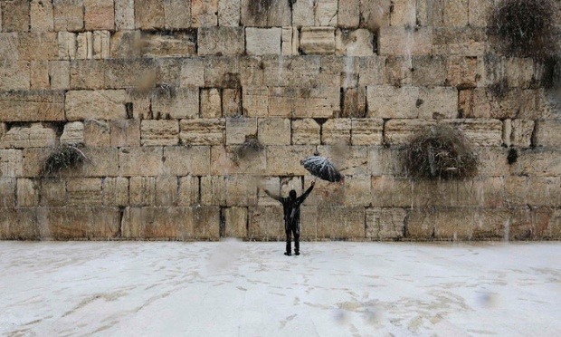 A man holding an umbrella walks as snow falls at the Western Wall in Jerusalem’s Old City. (Photo by Ammar Awad/Reuters via The Guardian)