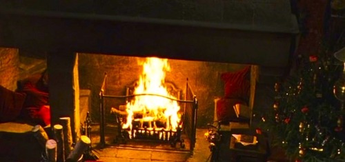 A toasty fire blazes in the Gryffindor Common Room beside a decorated tree during the Christmas holi