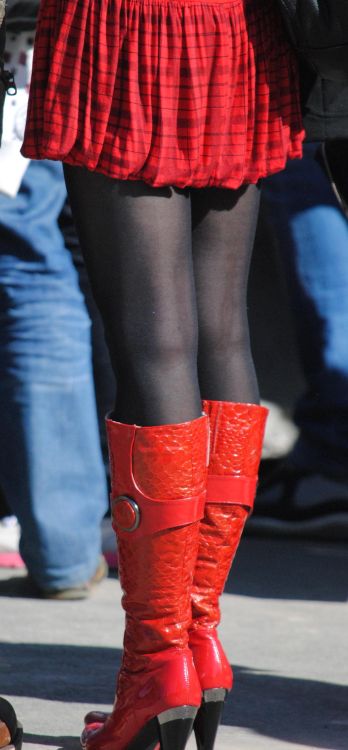 Pleated skirt, black pantyhose and red boots in the street.Woman in pantyhose