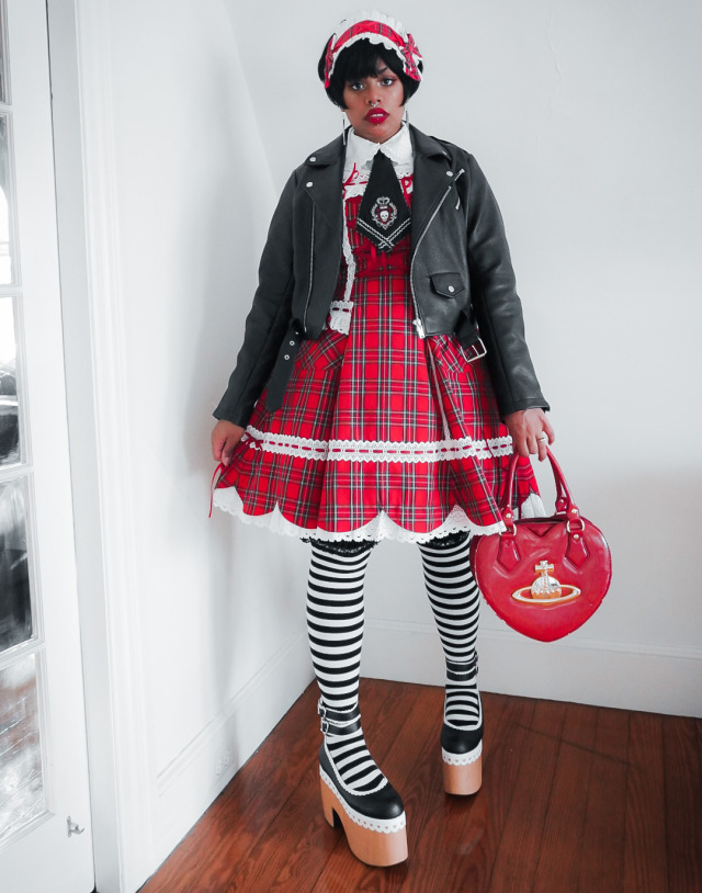 black person wearing a plaid lolita dress, black faux leather moto jack, cunky black and white shoes a plaid hair accessory
